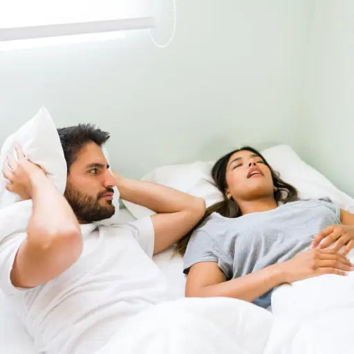 Woman snoring in bed while her male partner covers his ears with a pillow. Mouth Breathing and Increased Risk of Sleep Apnea