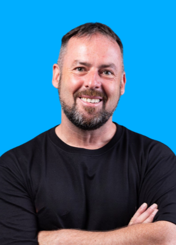 Patrick McKeown with arms crossed wearing a black shirt against a blue background